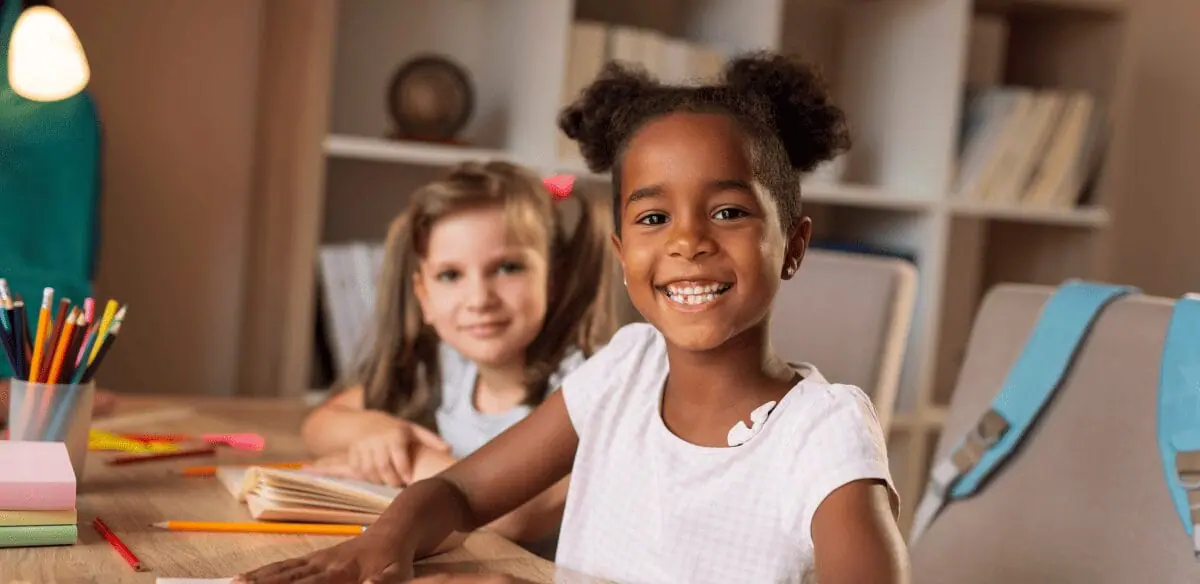 Dos niños sentados en una mesa, con las manos apoyadas en el escritorio, realizando juntos una actividad concentrada.