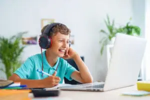 Un chico con auriculares está sentado en un escritorio, concentrado en su ordenador portátil, inmerso en su trabajo o entretenimiento.