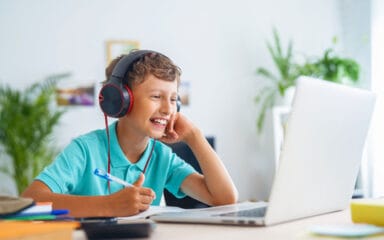 Un chico con auriculares está sentado en un escritorio, concentrado en su ordenador portátil, inmerso en su trabajo o entretenimiento.
