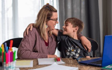 Una mujer y un niño están sentados en una mesa, ocupados con un ordenador portátil frente a ellos.