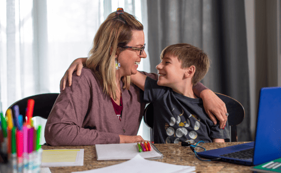 Una mujer y un niño están sentados en una mesa, ocupados con un ordenador portátil frente a ellos.