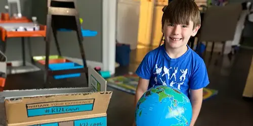 Un niño sostiene un globo terráqueo, situado delante de una caja, que simboliza la curiosidad y la exploración del mundo.