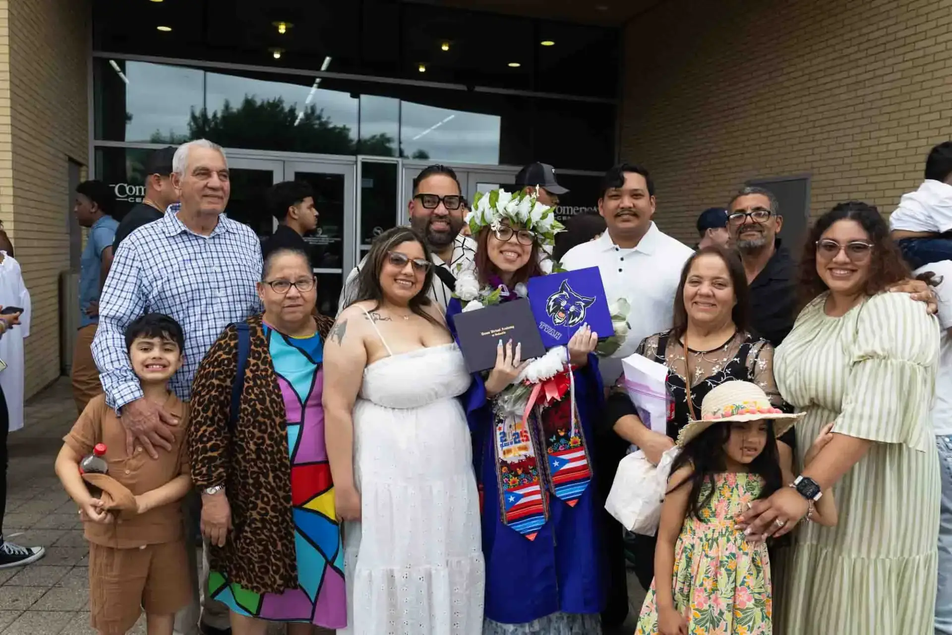 Una familia alegre se reúne para celebrar un graduado con toga y birrete azul, sosteniendo los diplomas. Las sonrisas y los coloridos atuendos reflejan orgullo y felicidad.
